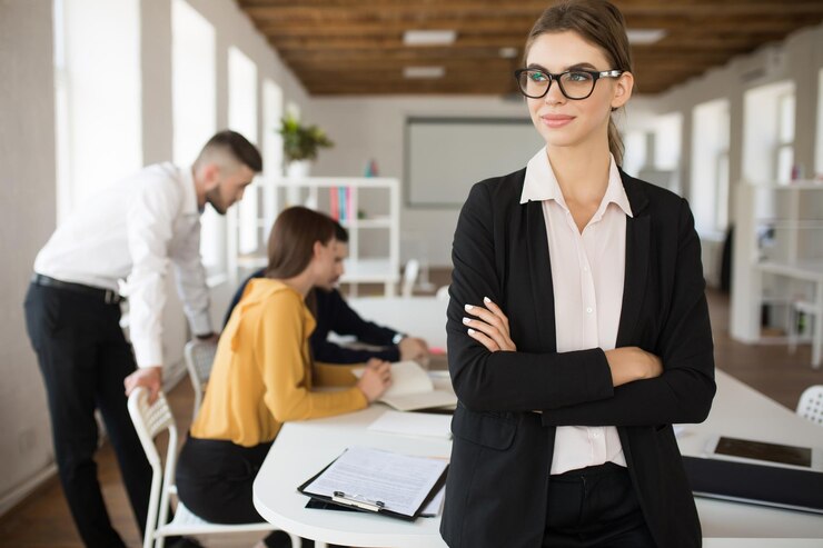 young smiling business woman eyeglasses shirt dreamily looking aside with folded hands while spending time office with colleagues background 574295 5669